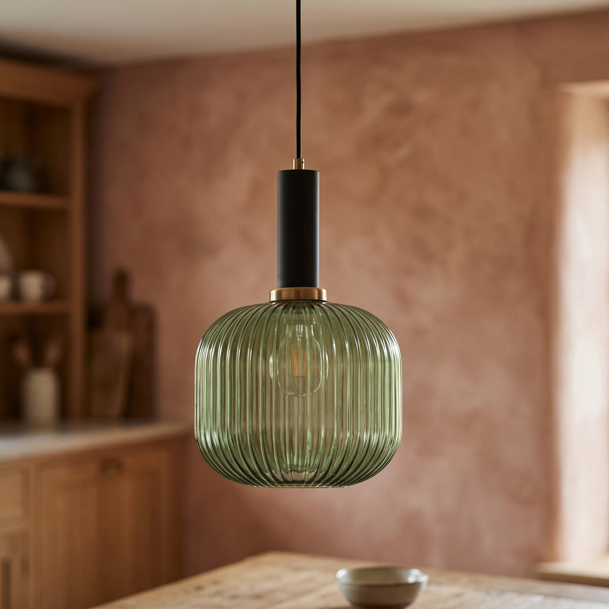 Kael green ribbed glass jar pendant light with a black cap against a terracotta clay kitchen wall and oak joinery
