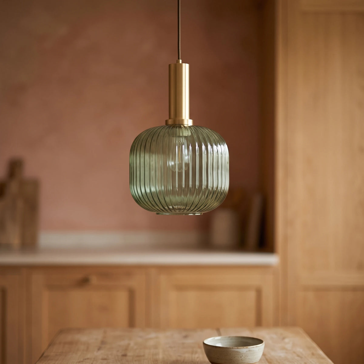 Kael green ribbed glass jar pendant light with a brass cap against a terracotta clay kitchen wall and oak joinery