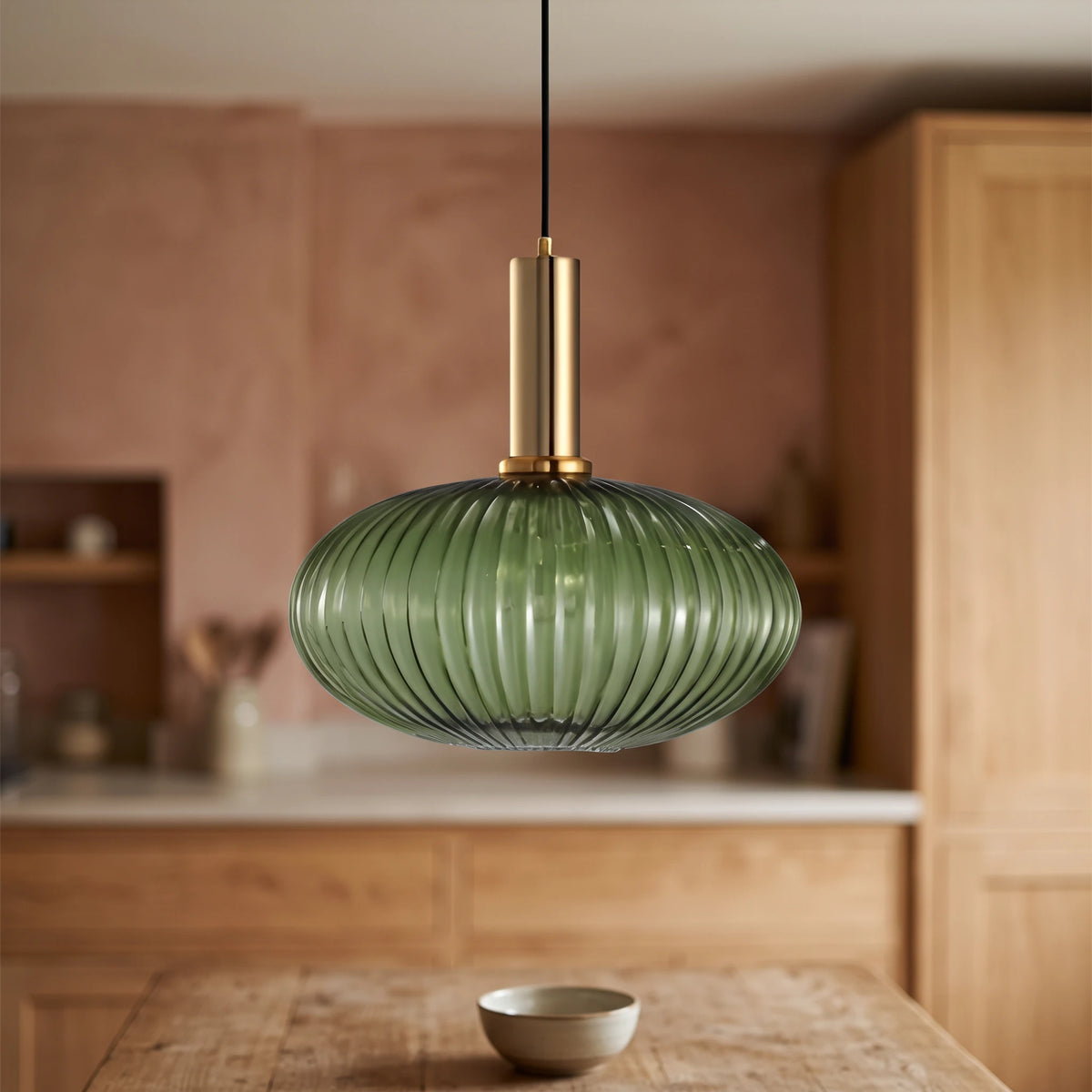 Kael wide green ribbed glass pendant light with a brass cap against a terracotta clay kitchen wall and oak joinery