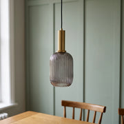 Kael smoked grey ribbed glass cylinder pendant light with a brass cap against a sage green panelled dining nook wall