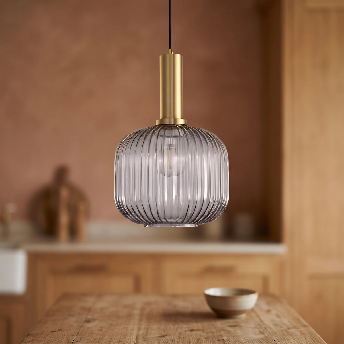 Kael smoked grey ribbed glass jar pendant light with a brass cap against a terracotta clay kitchen wall and oak joinery
