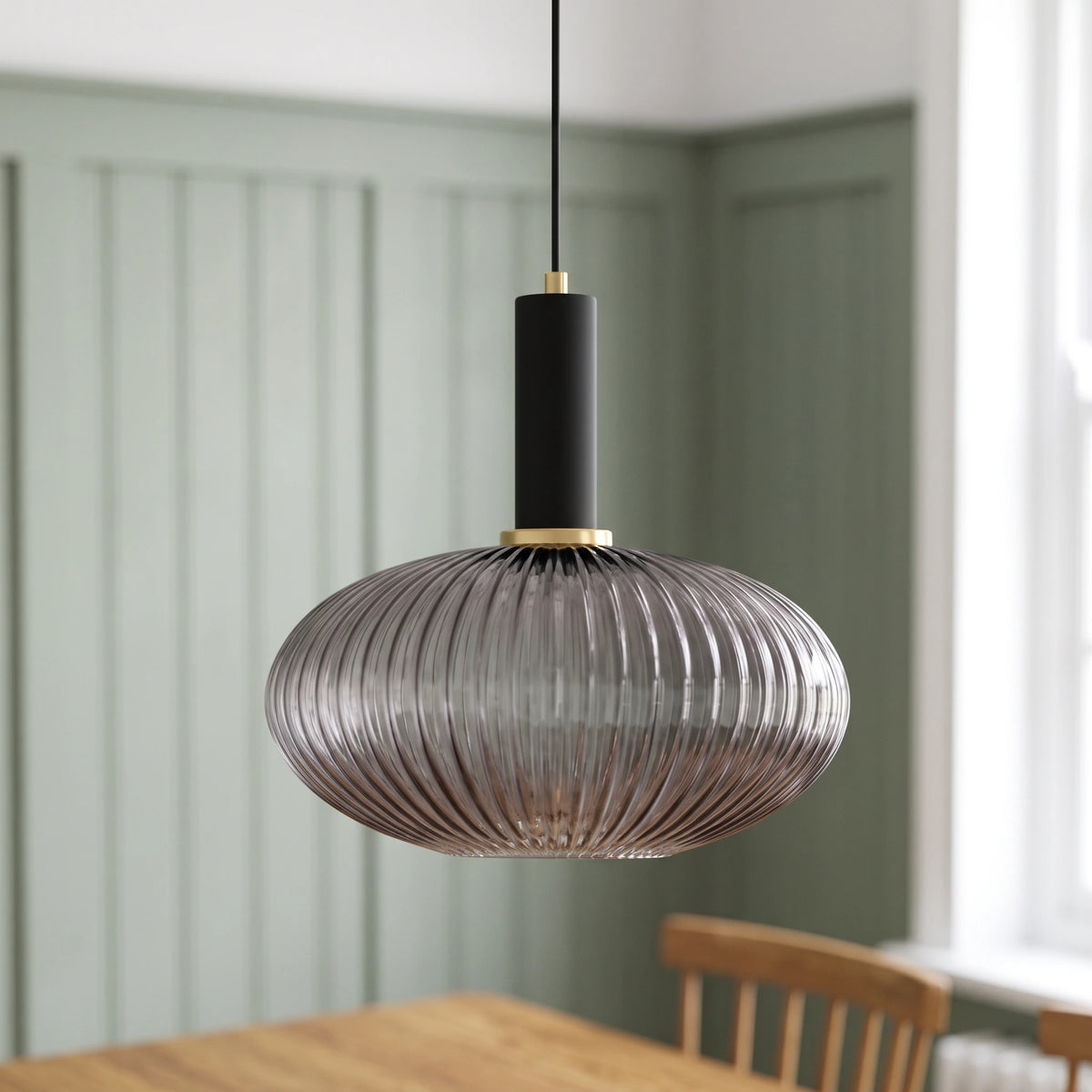 Kael wide smoked grey ribbed glass pendant light with a black cap against a sage green panelled dining nook wall