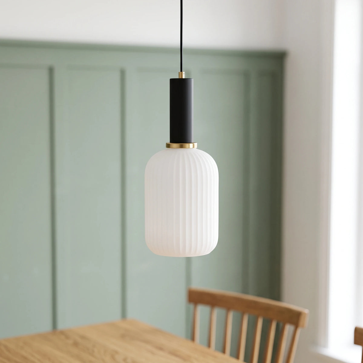 Kael white opal ribbed glass cylinder pendant light with a black cap against a sage green panelled dining nook wall