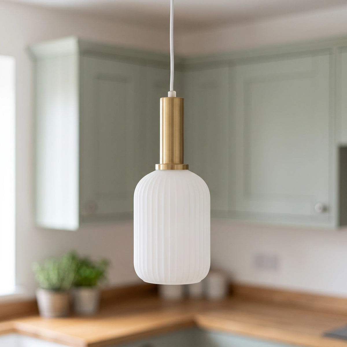 Kael white opal ribbed glass cylinder pendant light with a brass cap in front of sage green kitchen cabinets