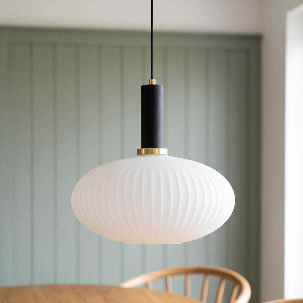 Kael wide white opal ribbed glass pendant light with a black cap against a sage green panelled dining nook wall