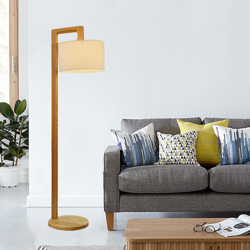 Modern wooden right-angle kelta floor lamp with a beige fabric shade standing next to a living room sofa