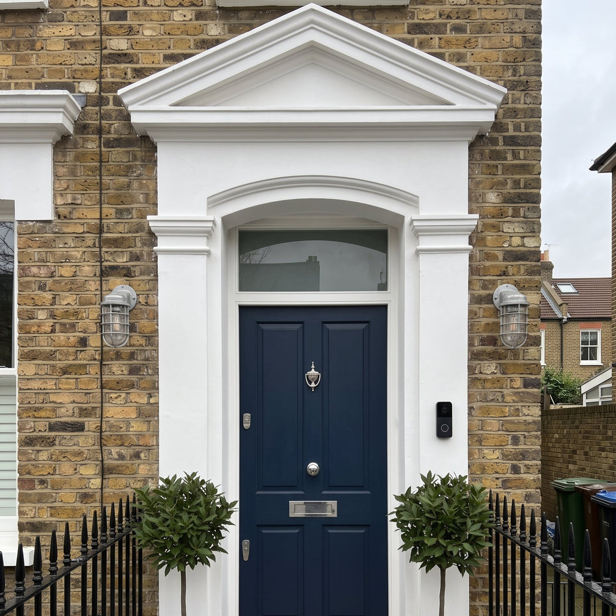 Laze cage guard bulkhead wall lights either side of a navy front door on a brick townhouse