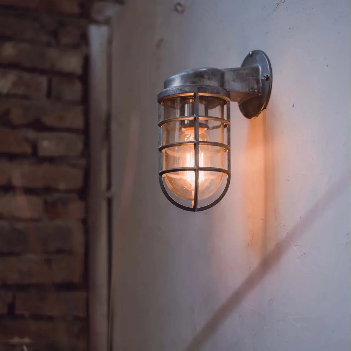 Laze silver cage guard bulkhead wall light lit beside a brick wall