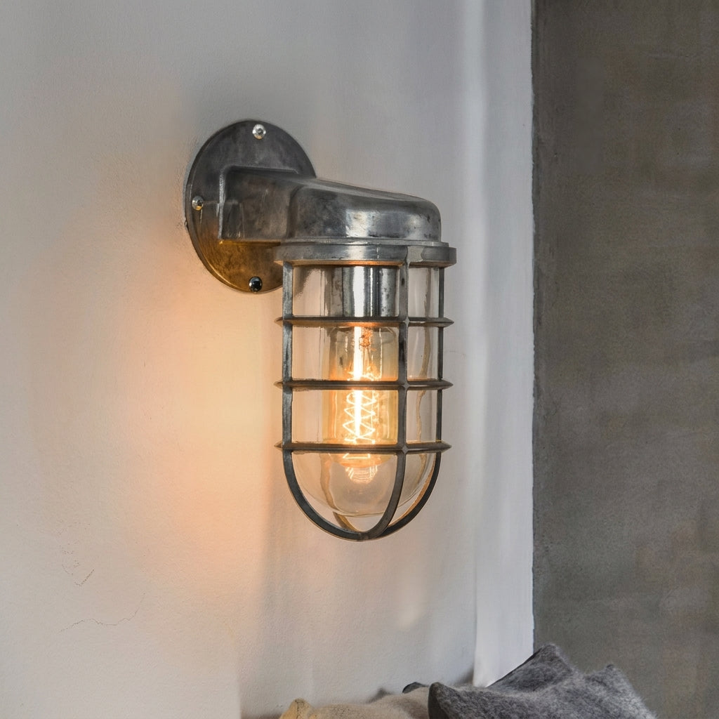 Laze silver cage guard bulkhead wall light lit on a white wall beside a concrete panel