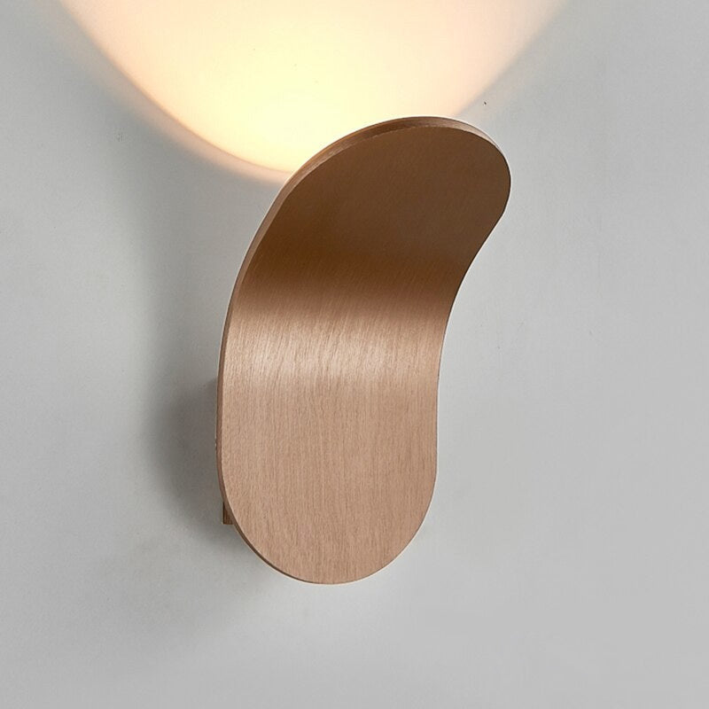 Champagne coloured curved LED lexi sconce glowing warmly against a light grey wall