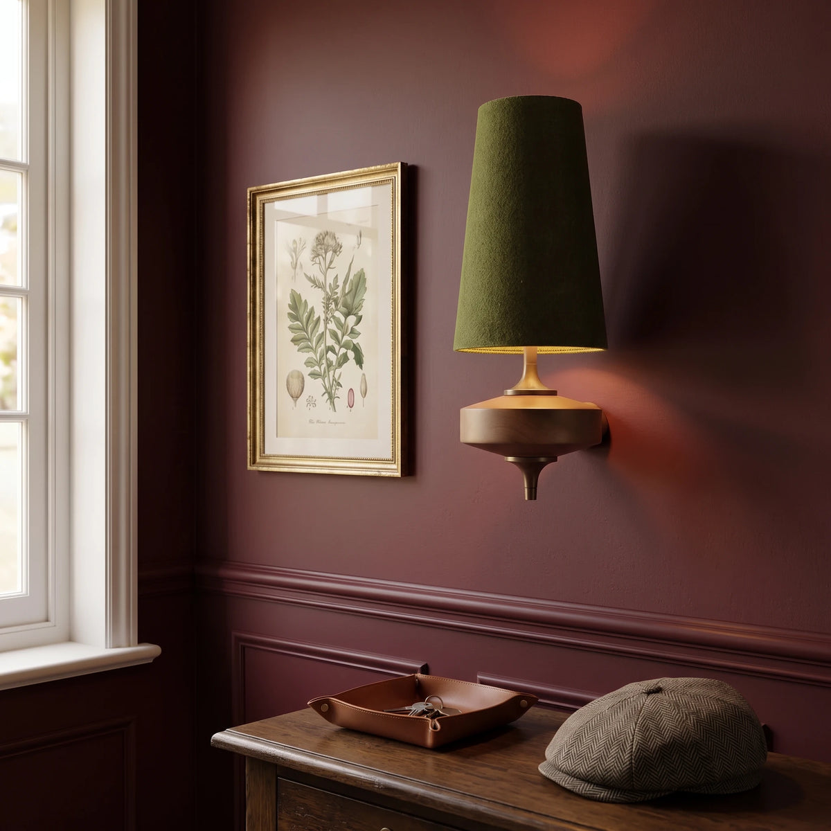 Lisk green fabric shade wall light on an oxblood wall beside a botanical print and an oak console with a flat cap