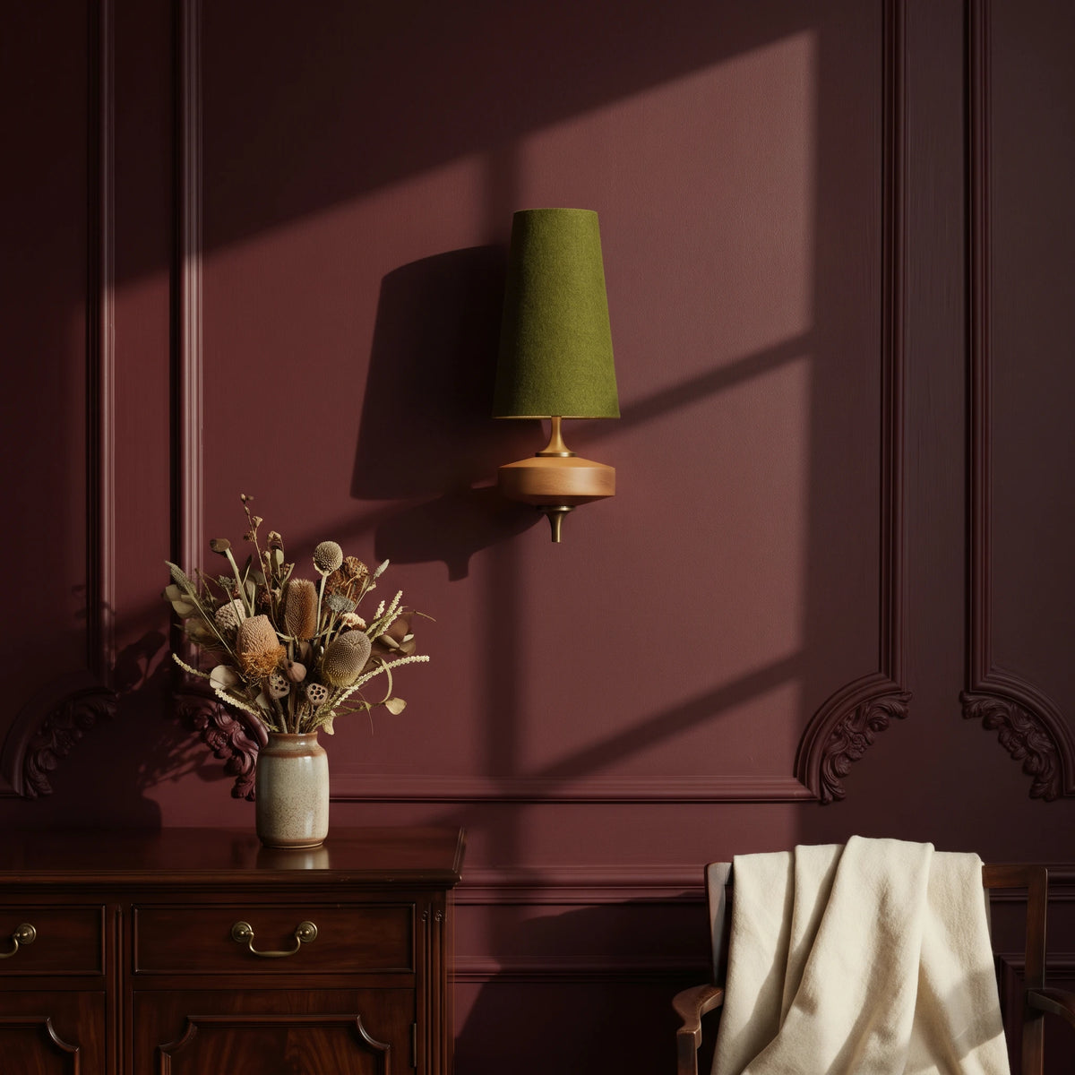 Lisk green fabric shade wall light on an oxblood panelled wall above a mahogany sideboard with dried flowers