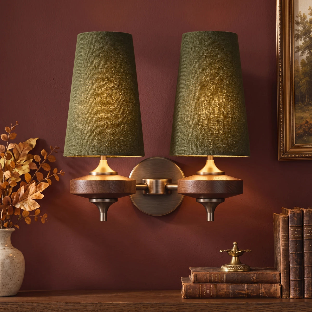 Close-up of the Lisk green 2-head fabric shade wall light on an oxblood wall with autumn leaves and a gilt frame