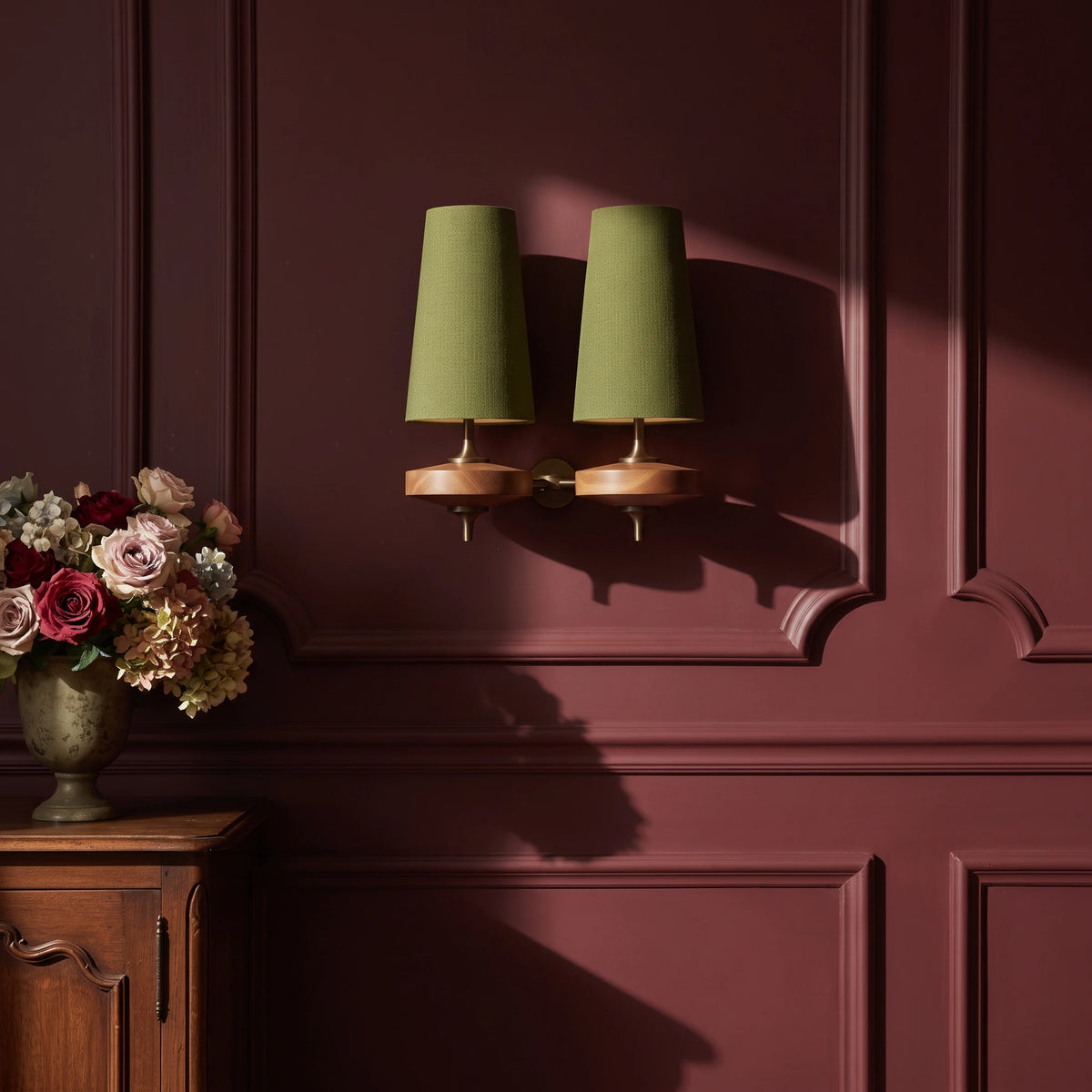 Lisk green 2-head fabric shade wall light on an oxblood panelled wall beside a vase of roses