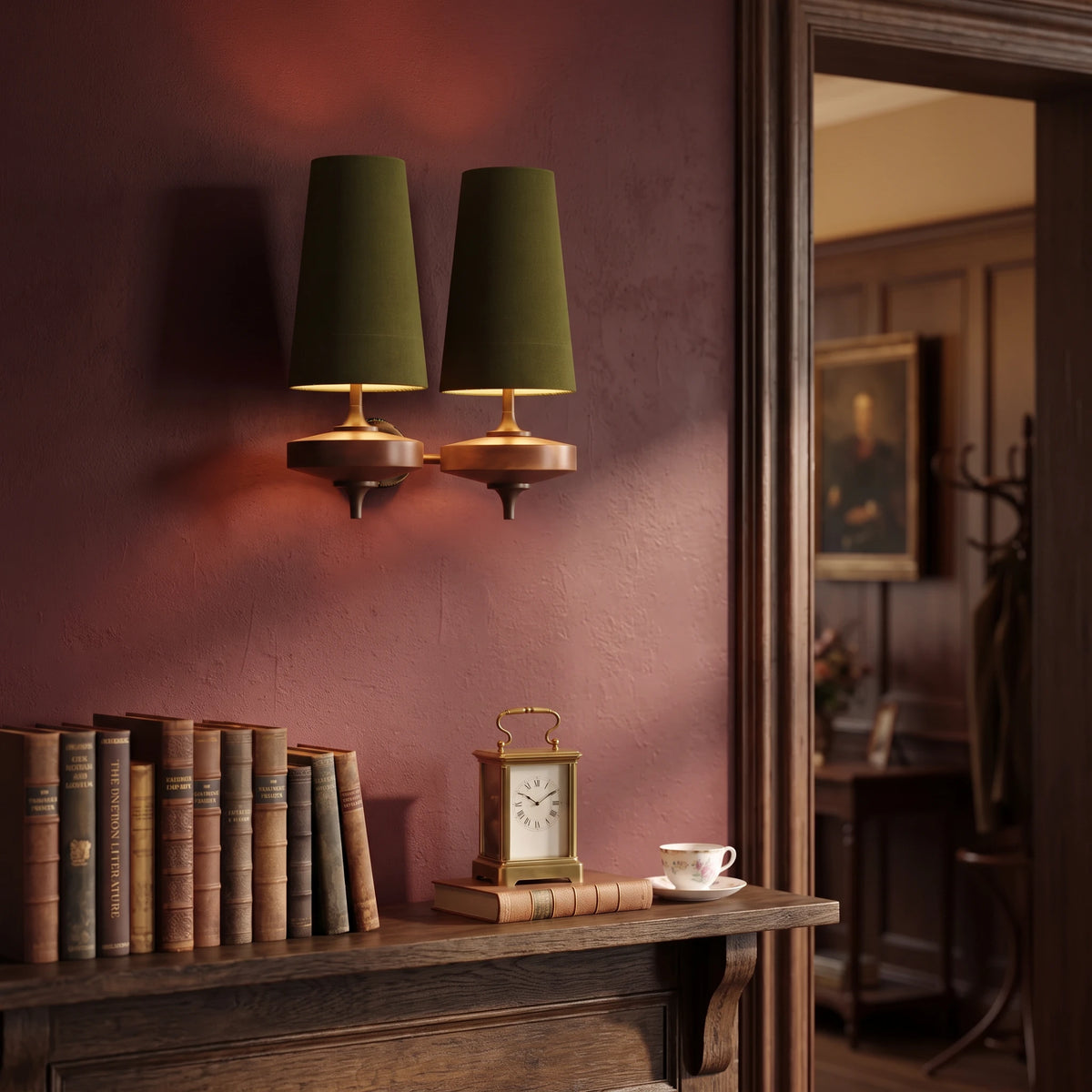 Lisk green 2-head fabric shade wall light on an oxblood wall above a mantel shelf with leather-bound books and a carriage clock