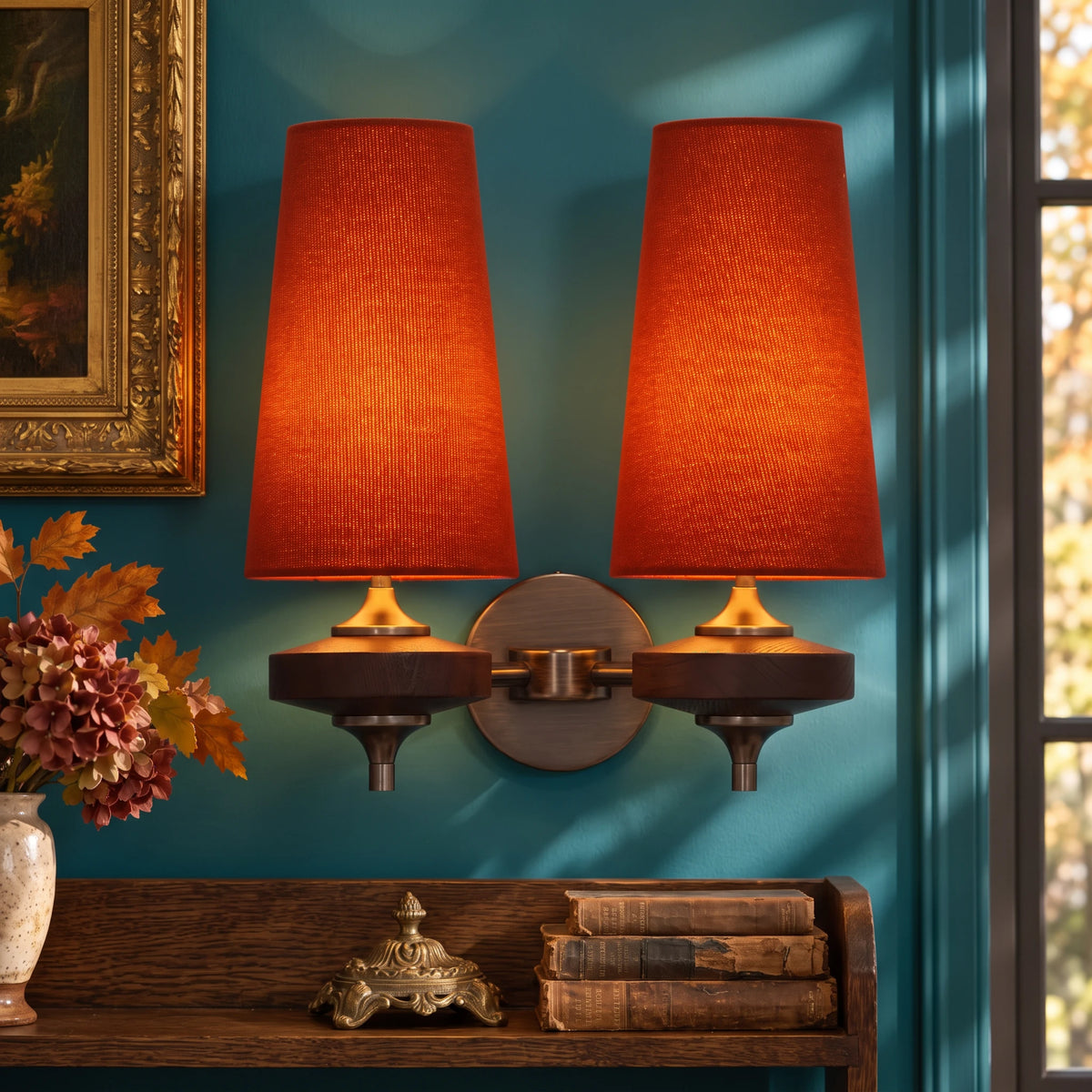 Close-up of the Lisk red 2-head fabric shade wall light on a deep teal wall above an oak shelf with old books