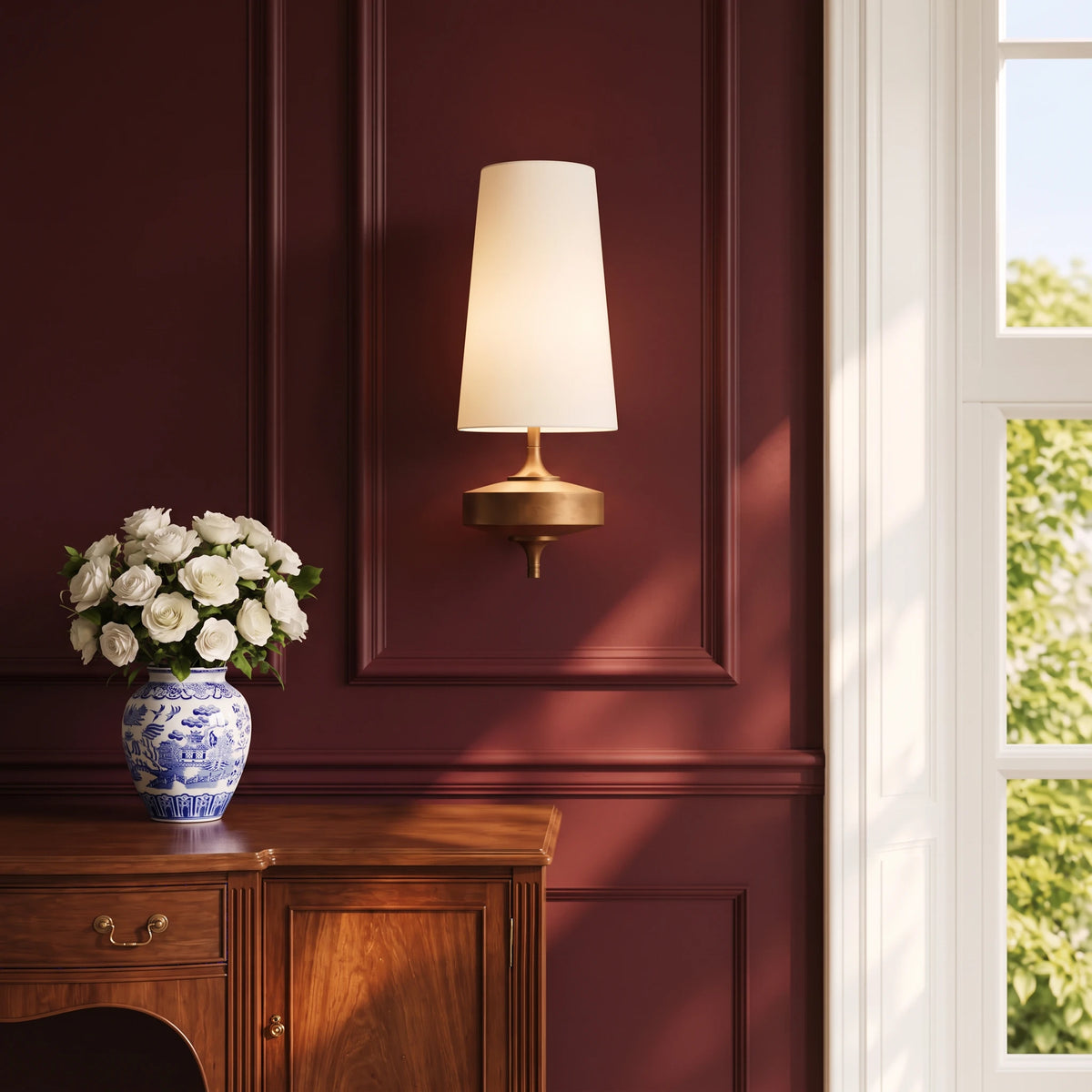 Lisk white fabric shade wall light on an oxblood panelled wall above an oak sideboard with a vase of white roses
