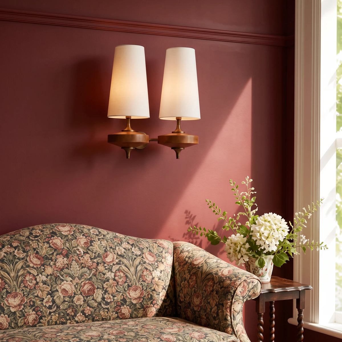 Lisk white 2-head fabric shade wall light on an oxblood wall above a chintz sofa