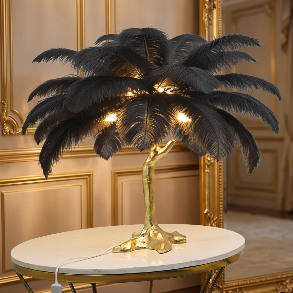 Lorne black ostrich feather lamp with a gold branch base on a marble side table against a champagne panelled wall