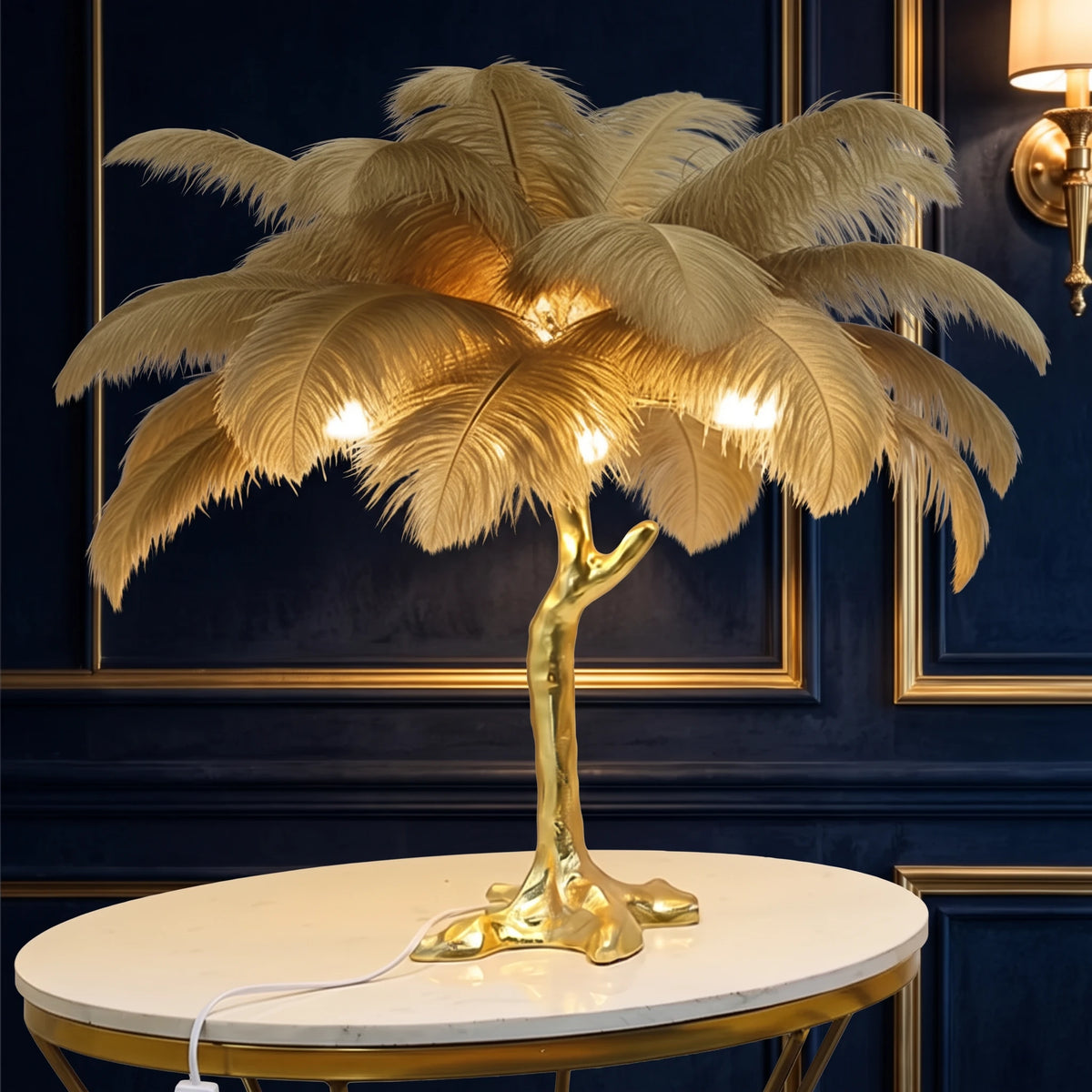 Lorne khaki ostrich feather lamp with a gold branch base on a marble side table against a navy velvet wall