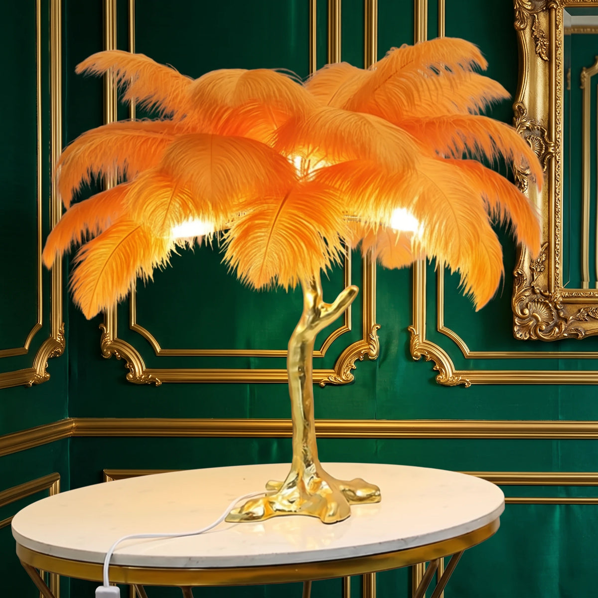 Lorne orange ostrich feather lamp with a gold branch base on a marble side table against an emerald green panelled wall