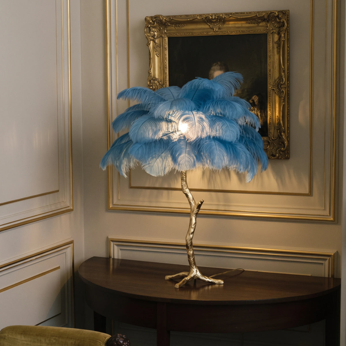 Lorne peacock blue ostrich feather lamp on a dark console table against ivory panelling and a gilt-framed painting