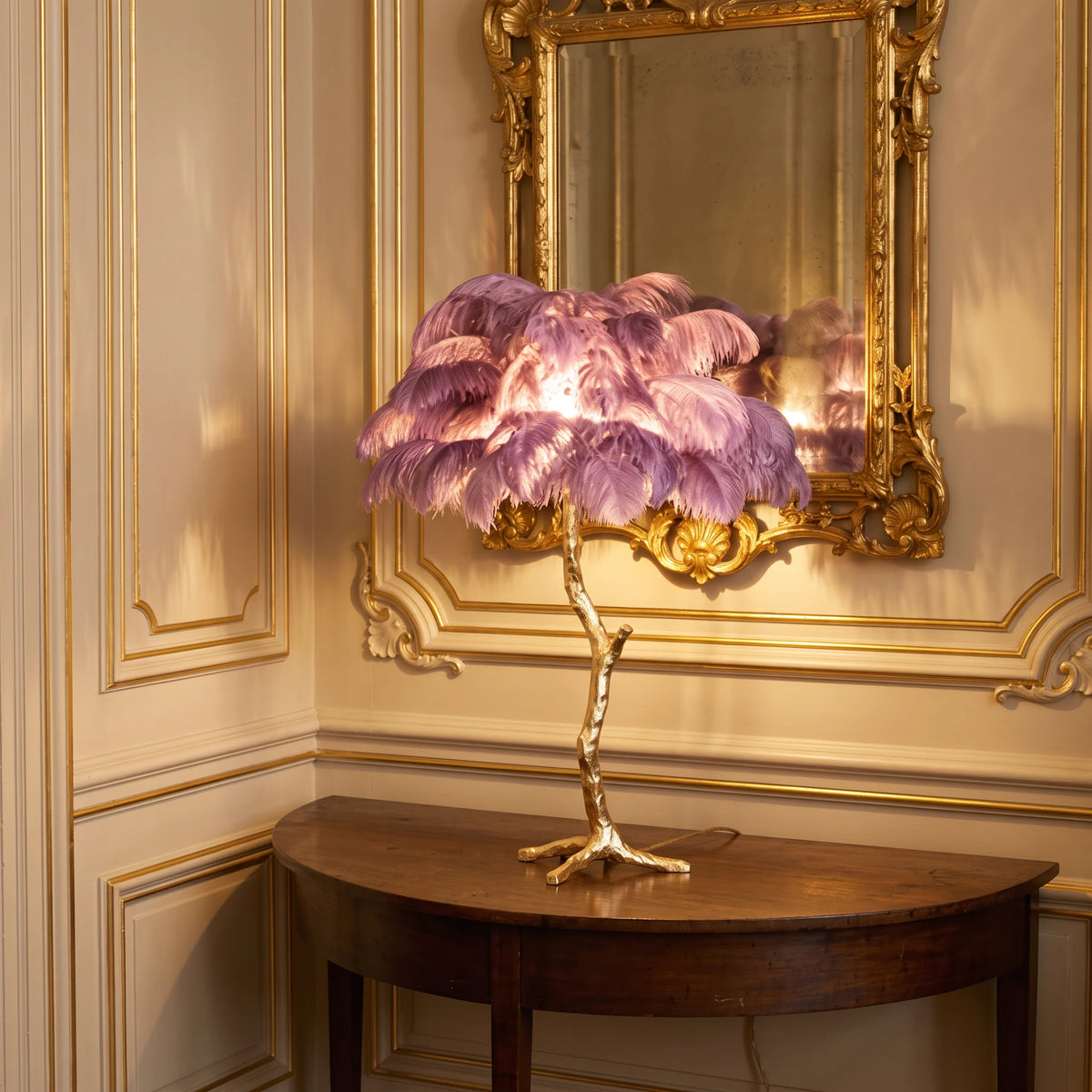 Lorne purple ostrich feather lamp on a dark console table beneath a gilt mirror in a champagne panelled room