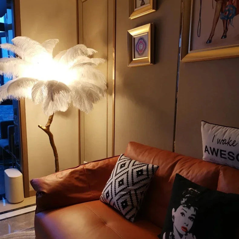 Lorne white ostrich feather floor lamp glowing beside a tan leather sofa under gilt-framed pictures