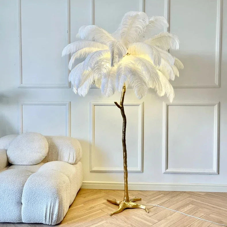 Lorne white ostrich feather floor lamp lit beside a cream bouclé sofa in a white panelled living room