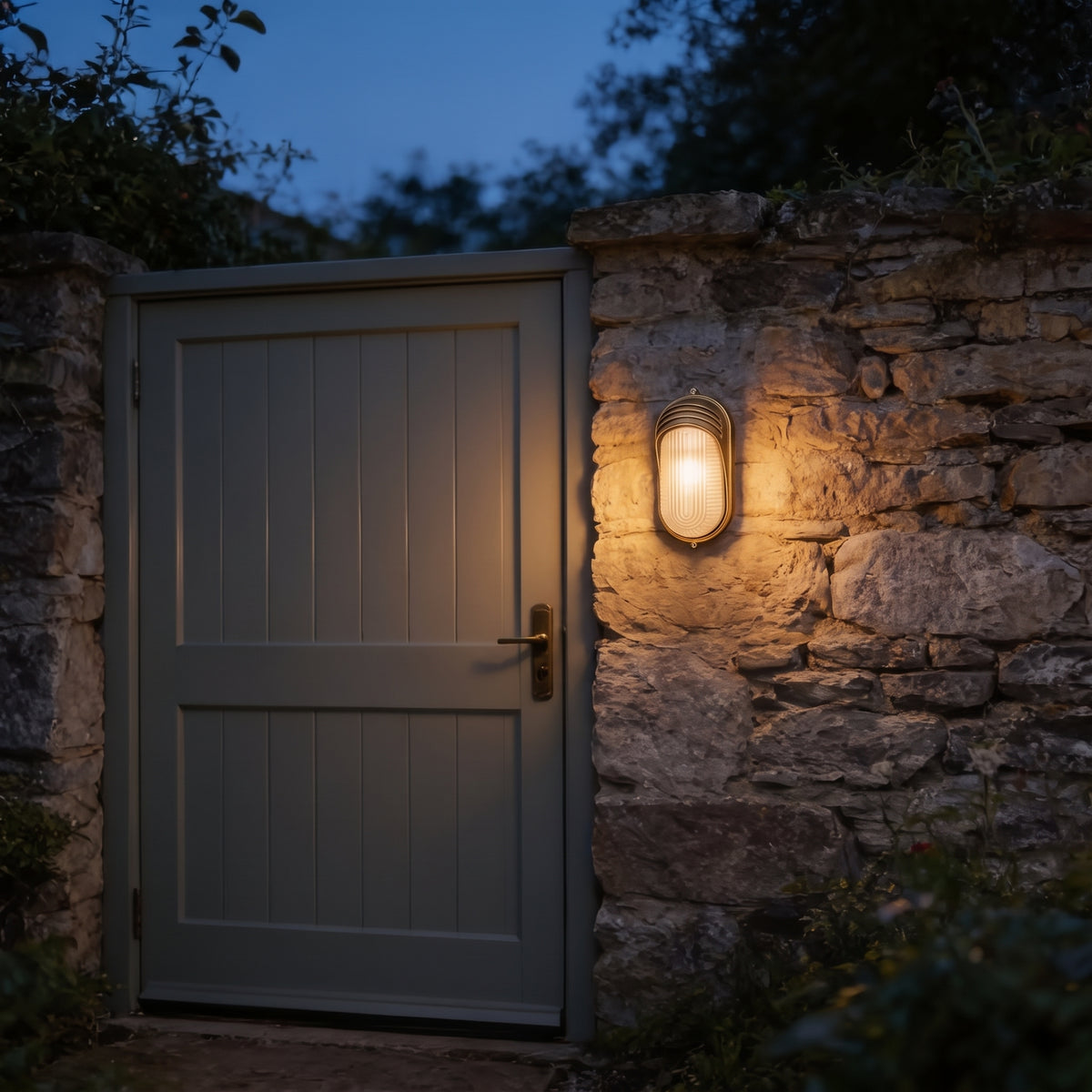 Lude bulkhead wall light lit beside a grey garden gate in a stone wall at dusk