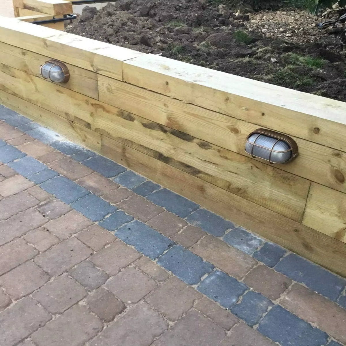 Lude bulkhead wall light installed on a timber sleeper wall above block paving