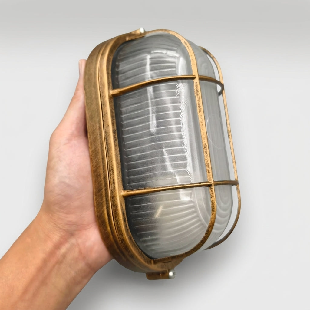 Hand holding the Lude cage guard bulkhead wall light at an angle showing the ribbed glass shade