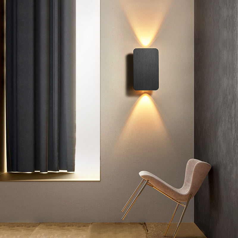 Black up and down mazka lighting rectangular wall sconce illuminating a sleek, modern reading corner