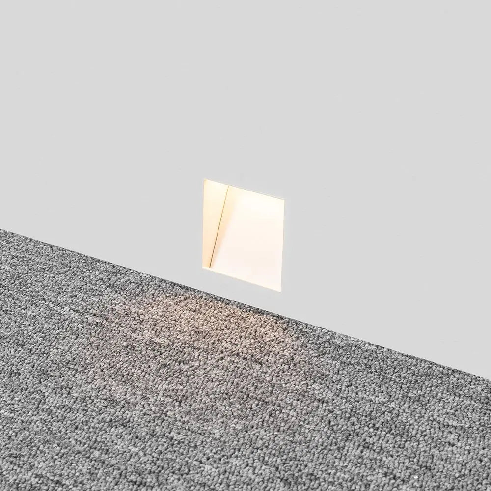 Melte white trimless recessed LED wall light set low in a grey wall above carpet