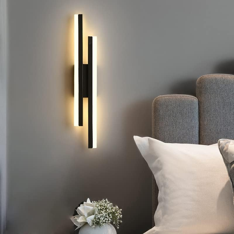 Asymmetrical milor black linear LED sconce illuminating the wall next to a modern grey tufted headboard