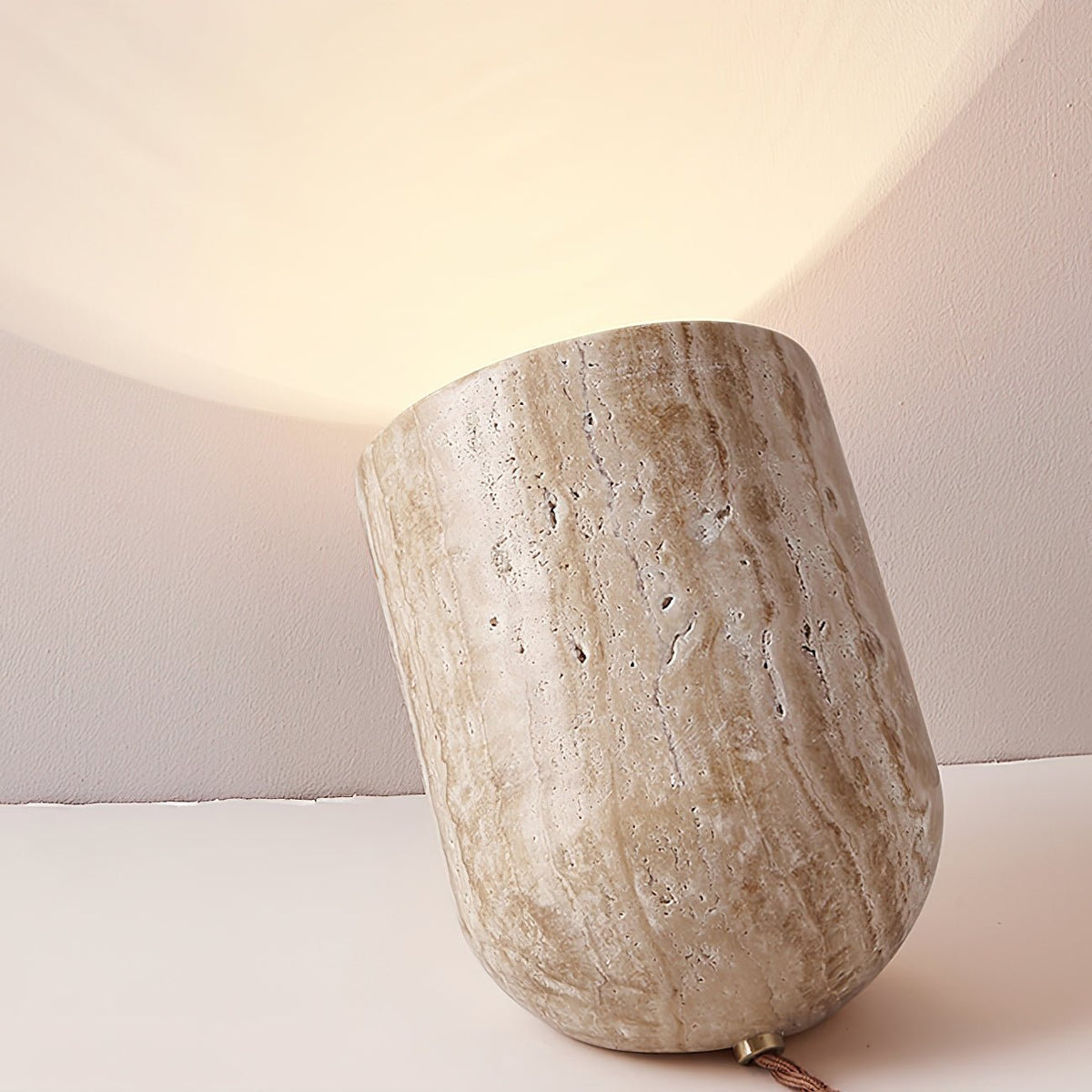Organic stone misa bedside lamp carved from travertine, resting on a table and casting a soft upward light