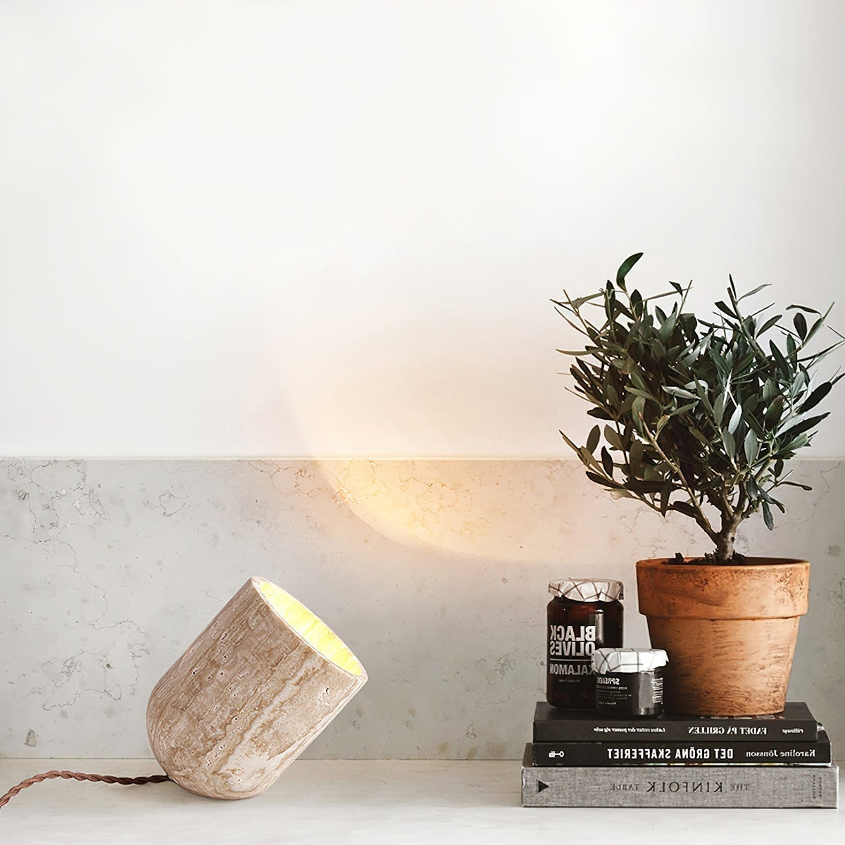 Natural travertine misa table lamp styled on a surface next to books and a small potted plant in a modern home