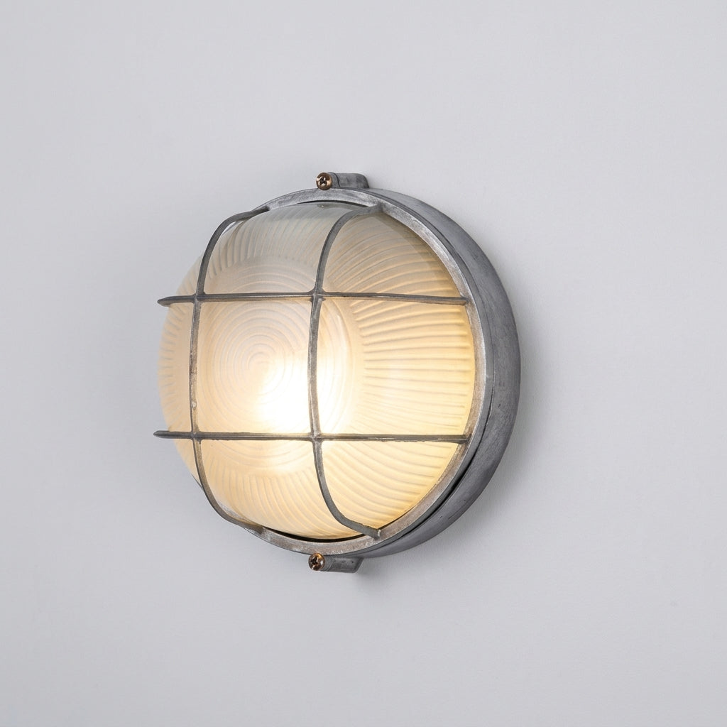 A vintage-style industrial outdoor wall light with a ribbed glass globe and a protective metal cage, shown illuminated against a plain light grey wall.
