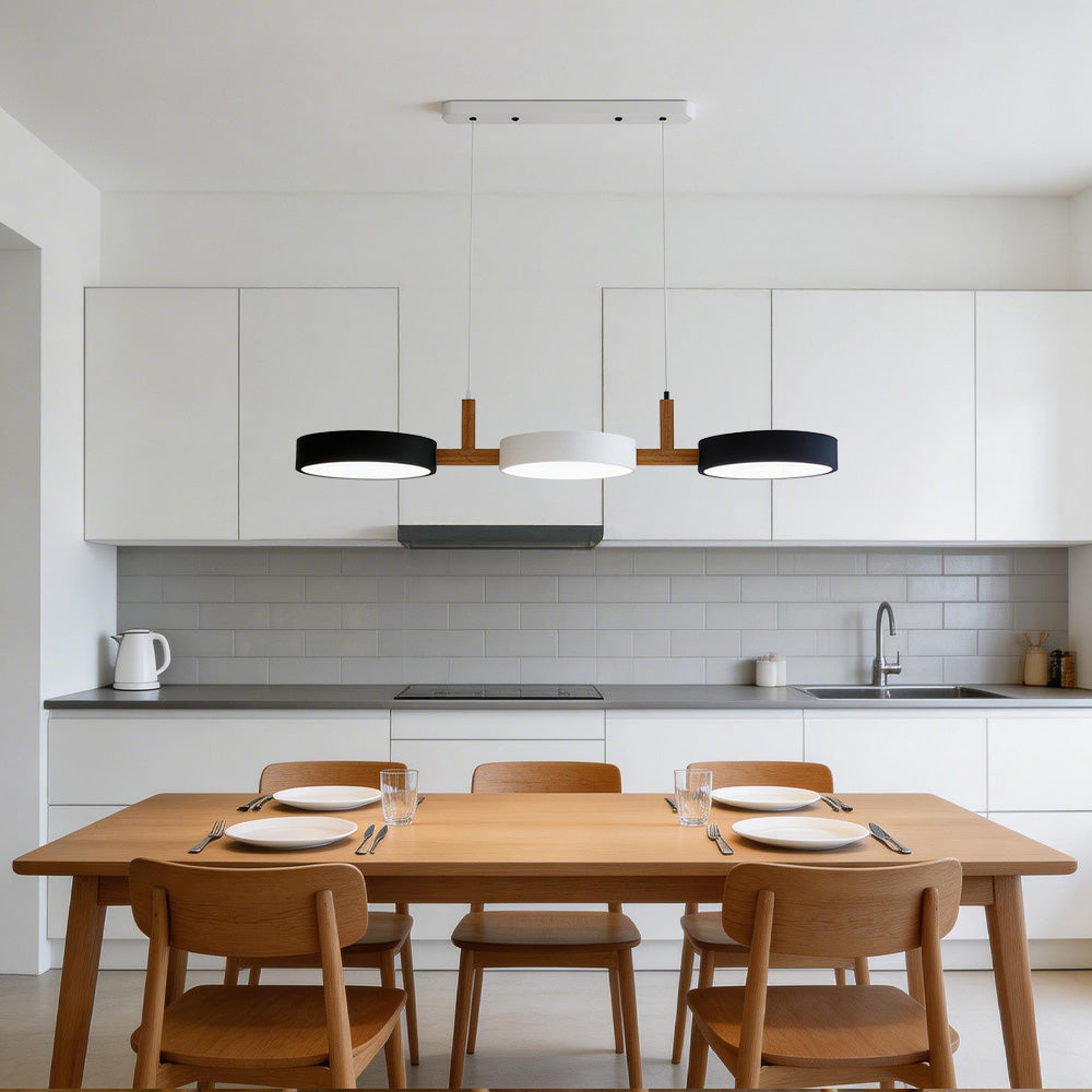 Black, white, and black 3-head nohit pendant illuminating a long wooden dining table in a minimalist kitchen