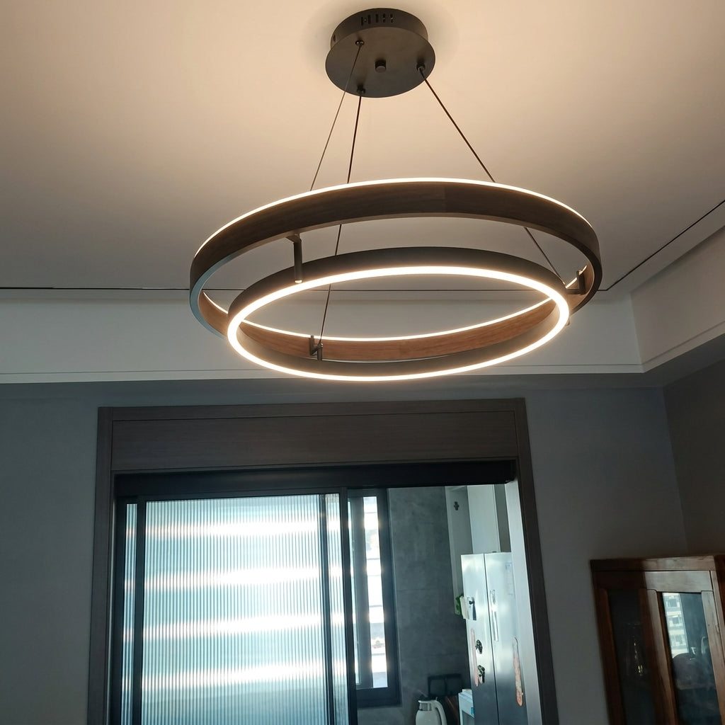 Close-up of the Nyles two-ring LED chandelier and black ceiling canopy glowing warm white