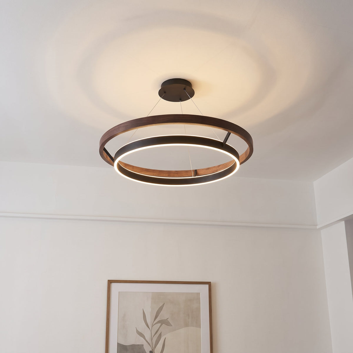 Nyles two-ring wood-grain LED chandelier on a white ceiling above a framed neutral print