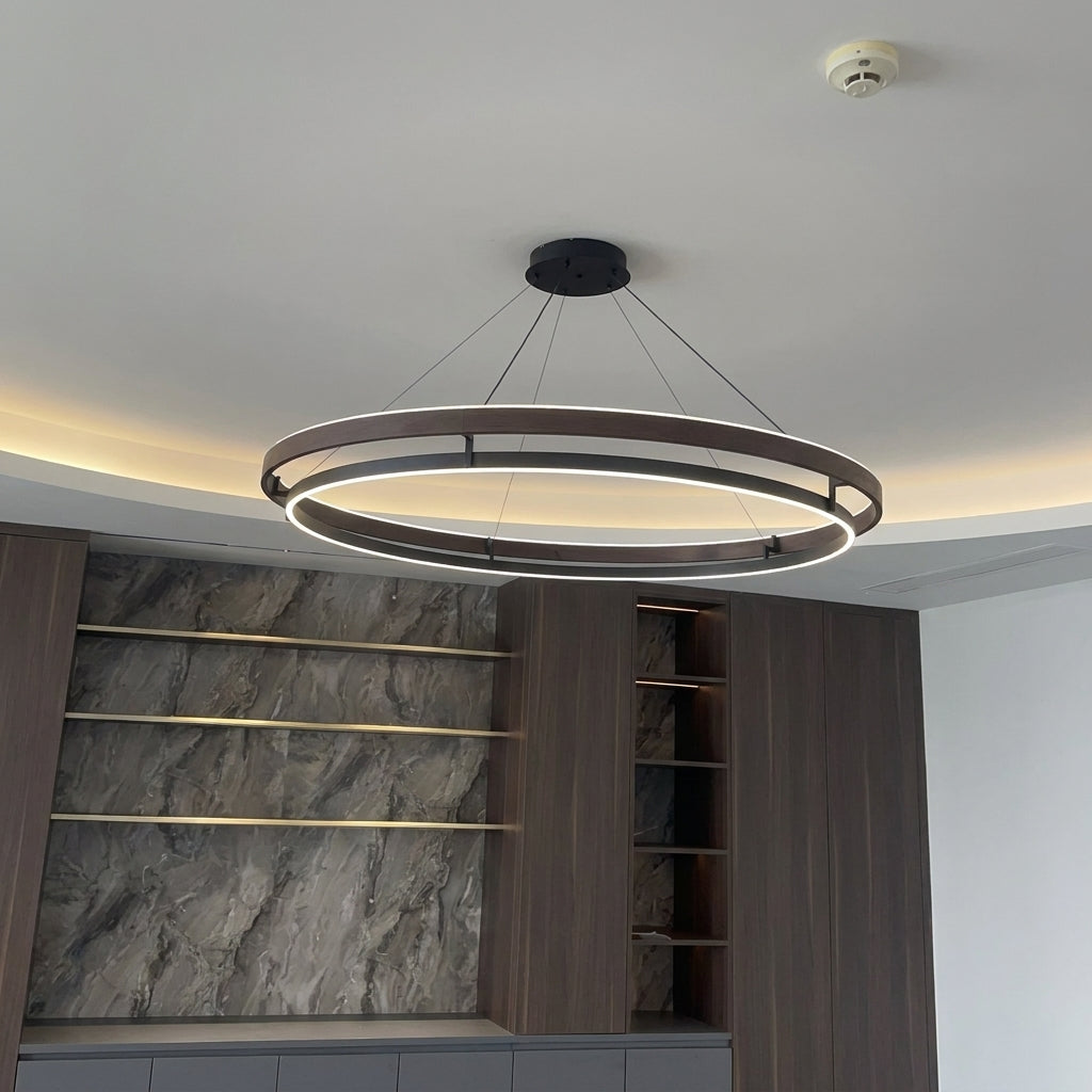 Nyles two-ring LED chandelier on a ceiling with warm coving light above a stone-effect panel wall and shelving