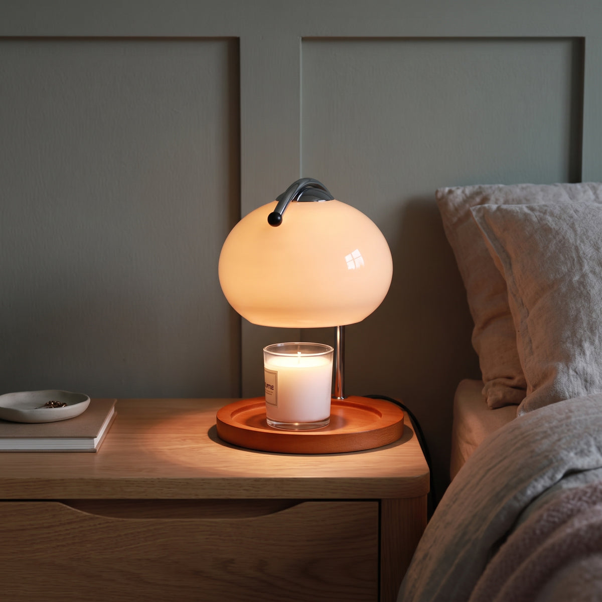 Ondo milky white glass candle warmer lamp glowing on an oak bedside table in an evening bedroom