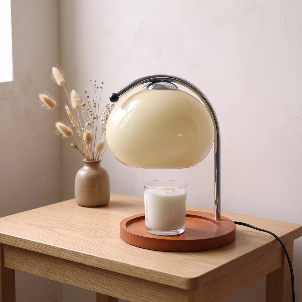 Ondo milky white glass candle warmer lamp on an oak side table next to a vase of dried grasses