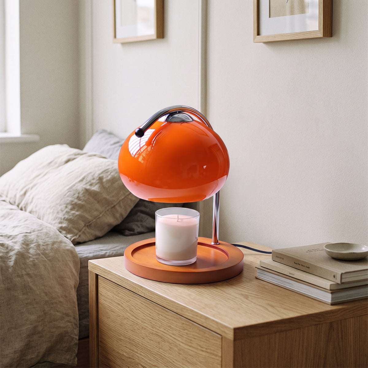 Ondo orange glass candle warmer lamp on an oak bedside table beside a stack of books