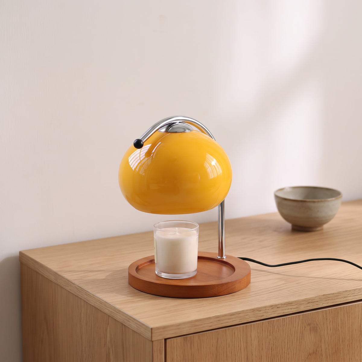 Ondo yellow glass candle warmer lamp on an oak sideboard beside a small ceramic bowl