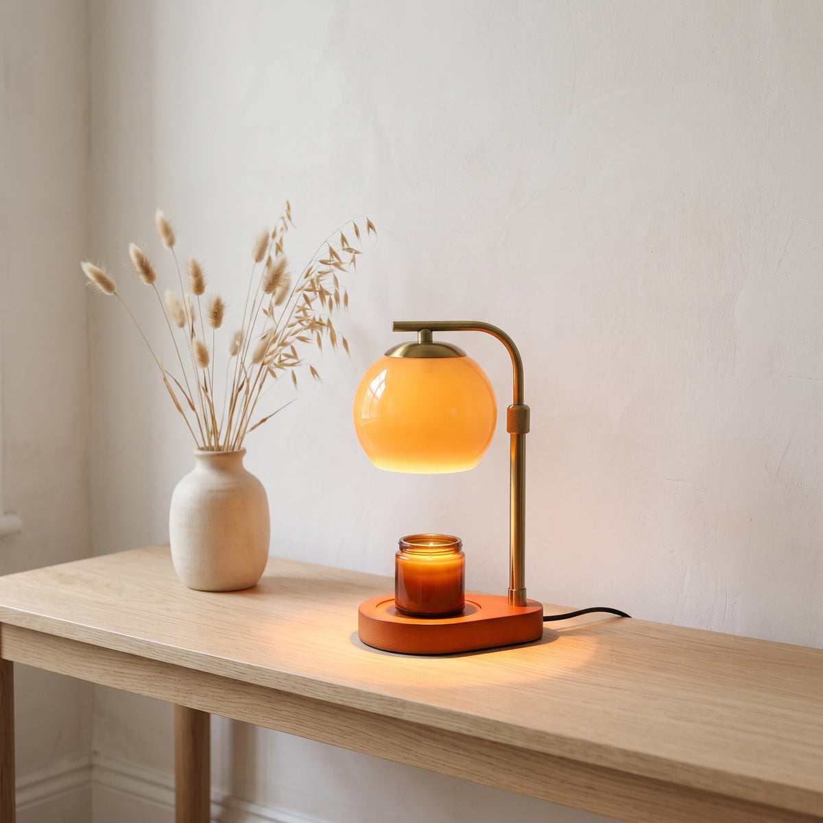 Orsa brown glass globe candle warmer lamp on an oak console table with dried grasses