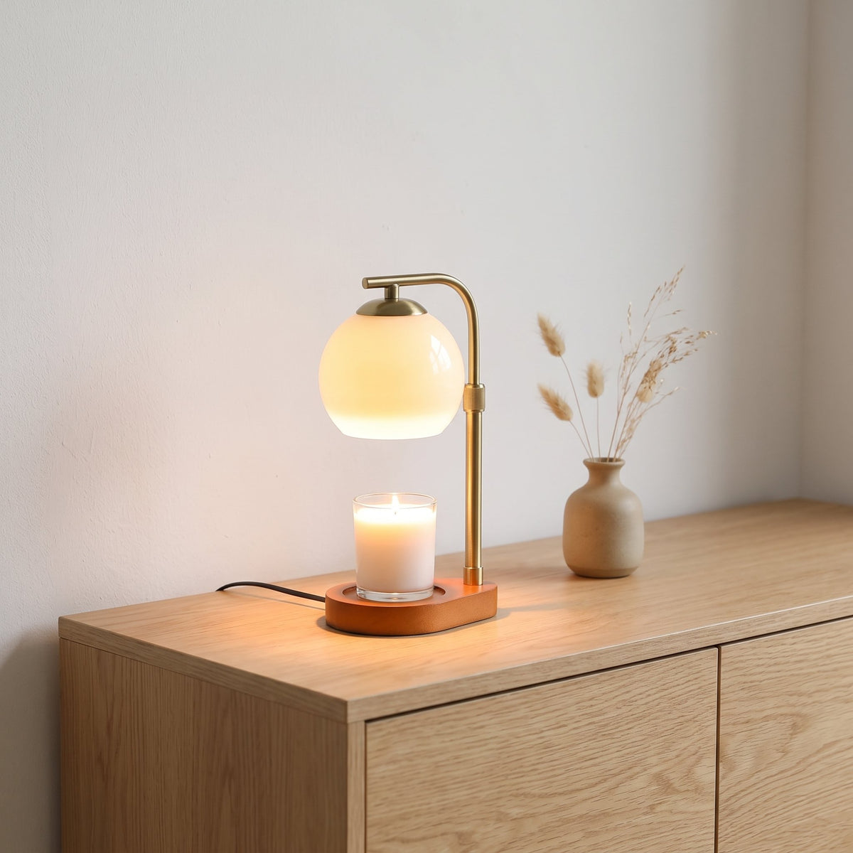 Orsa glass globe candle warmer lamp on an oak sideboard beside a vase of dried grasses