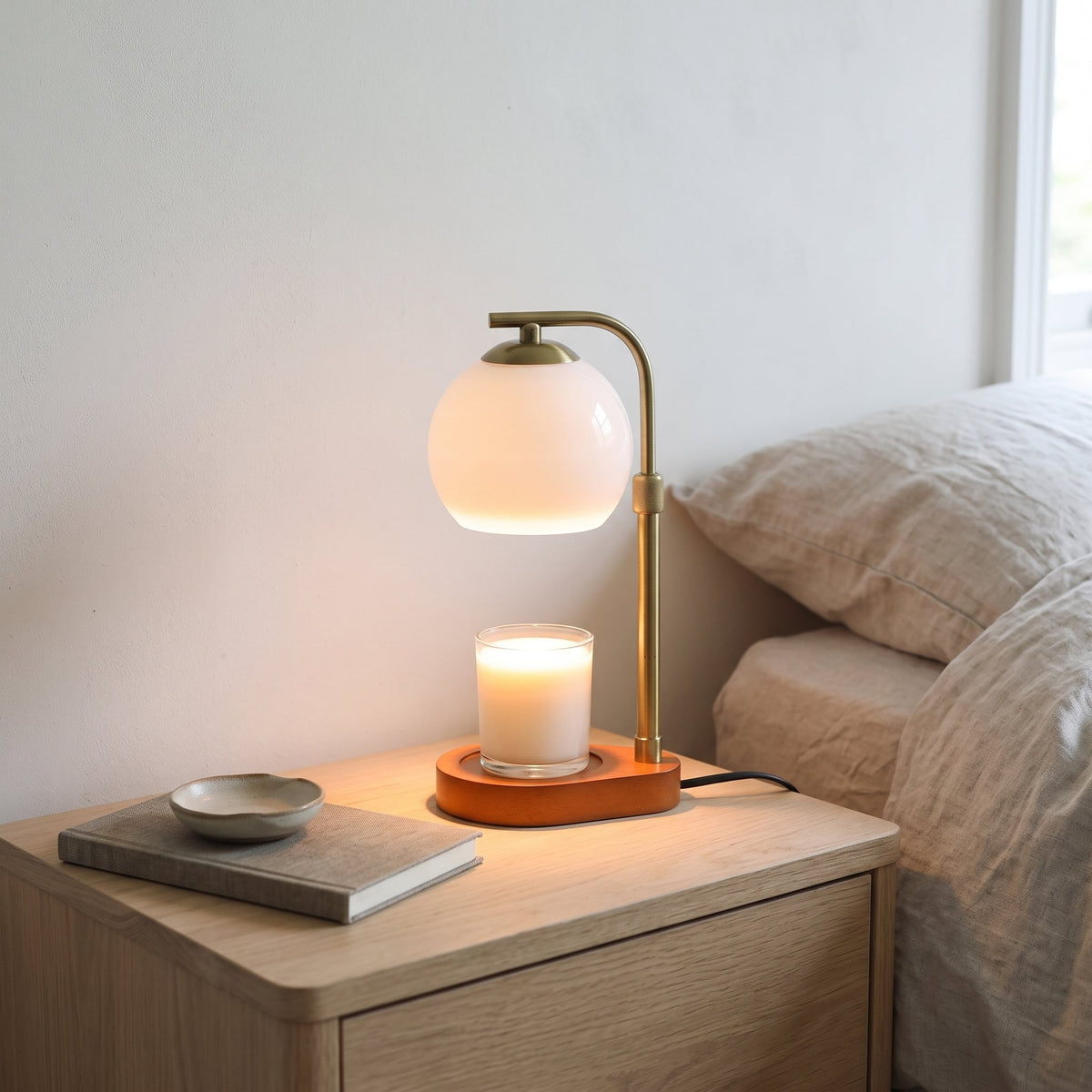 Orsa white glass globe candle warmer lamp on an oak bedside table next to a bed