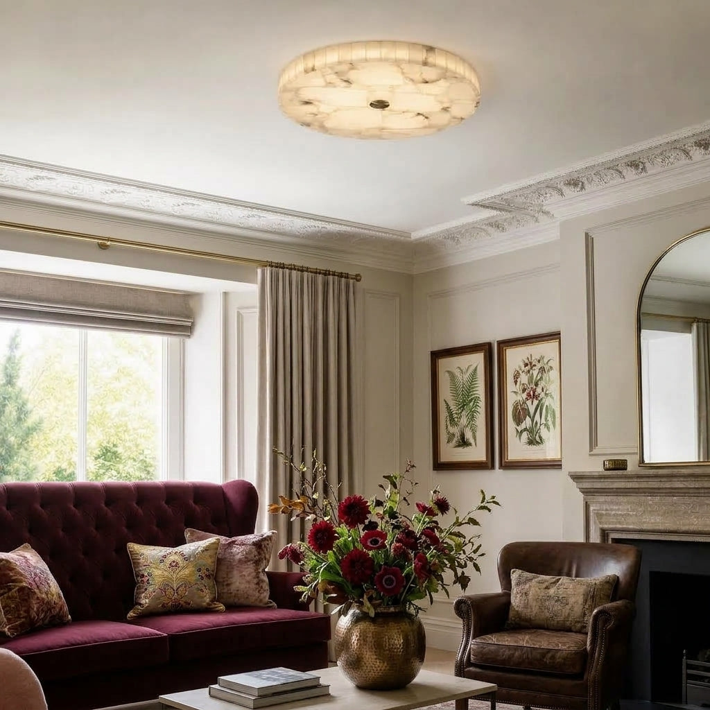 A round ceiling light fixture with a textured, marbled tones, glowing in a classic, elegant living room with a burgundy sofa, brown leather armchair, and fireplace.